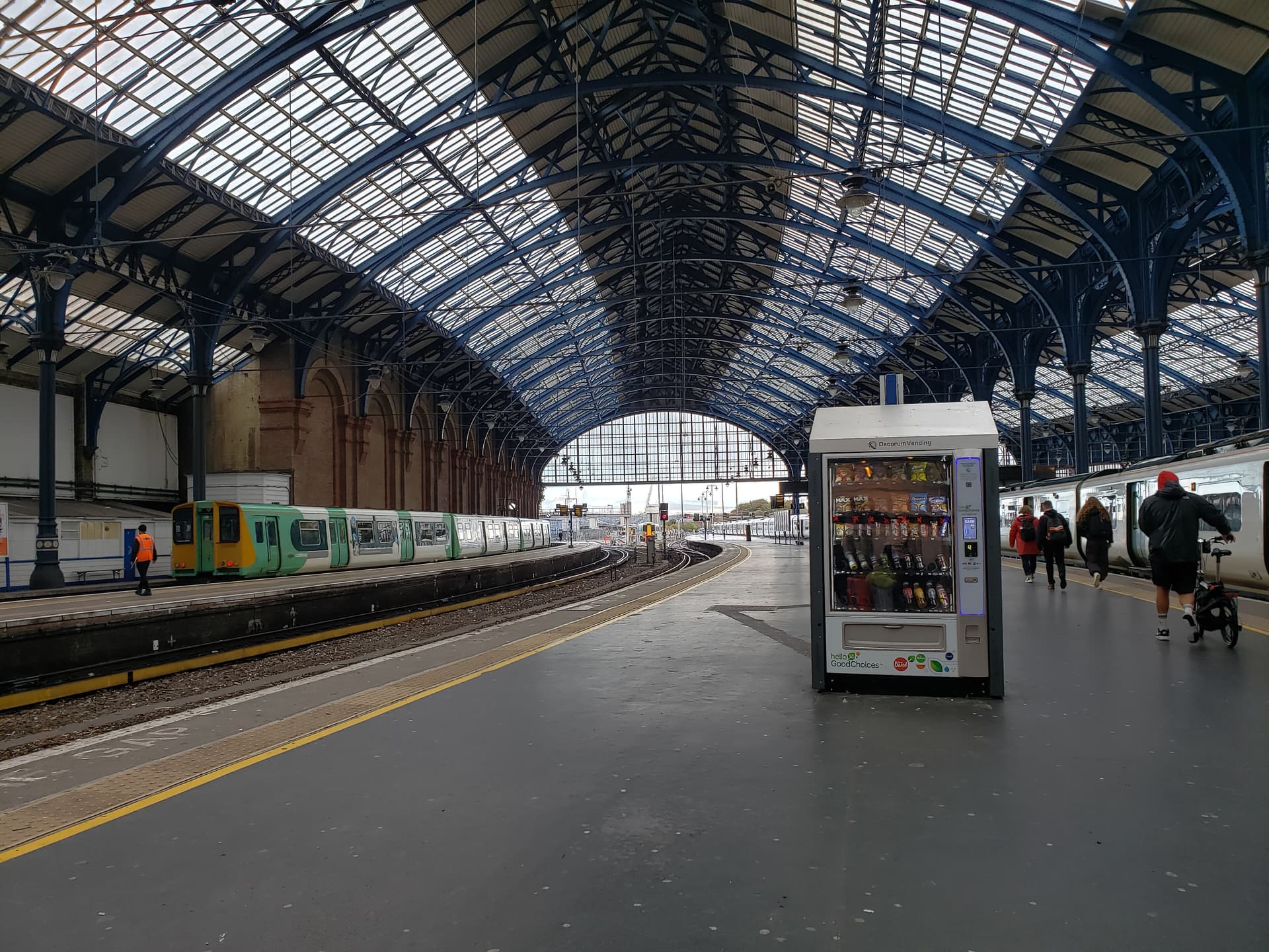 Curved blue iron and glass roof over platforms at Brighton station, with a green and white train and vending machine