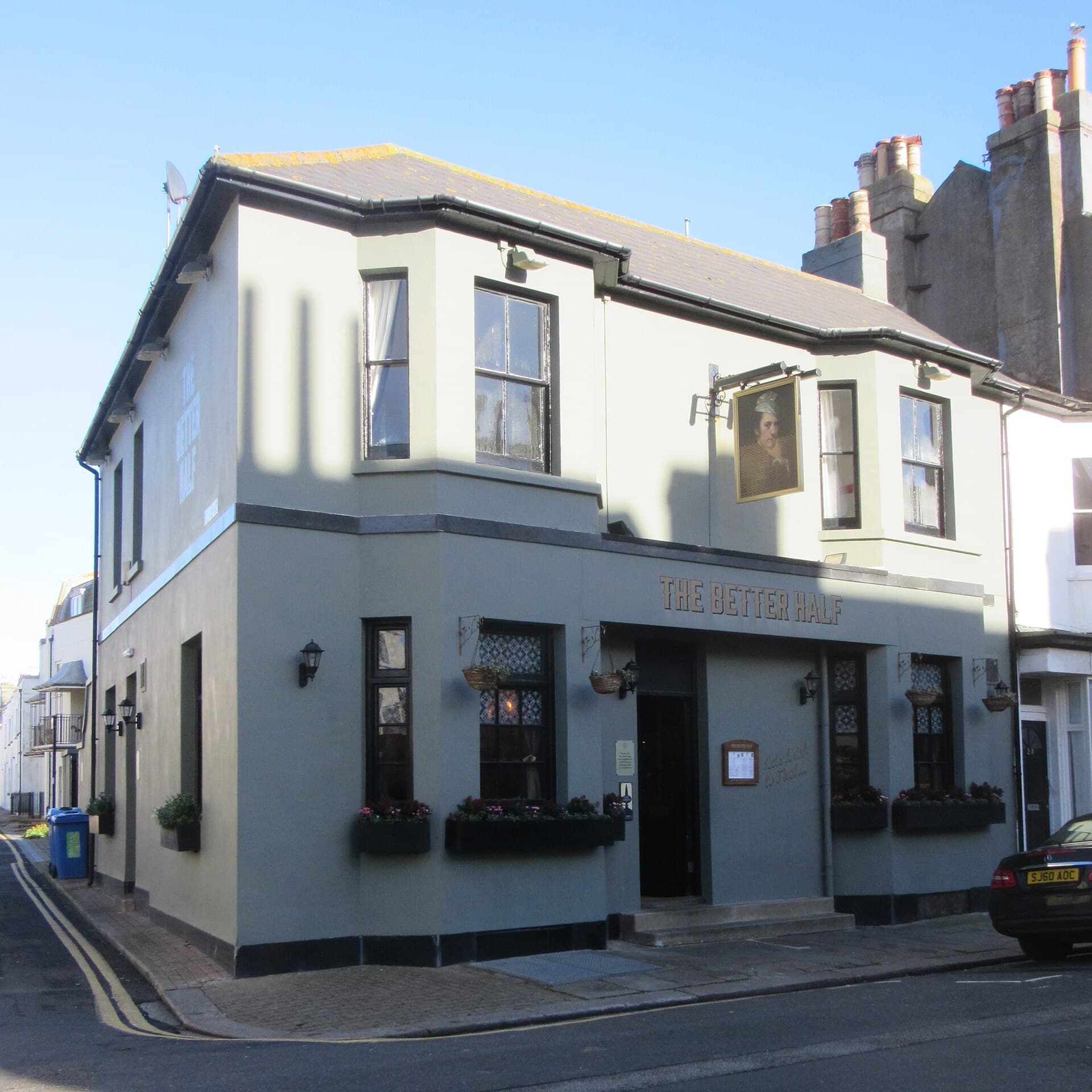 Corner pub called The Better Half with grey painted walls, hanging flower baskets and a portrait pub sign